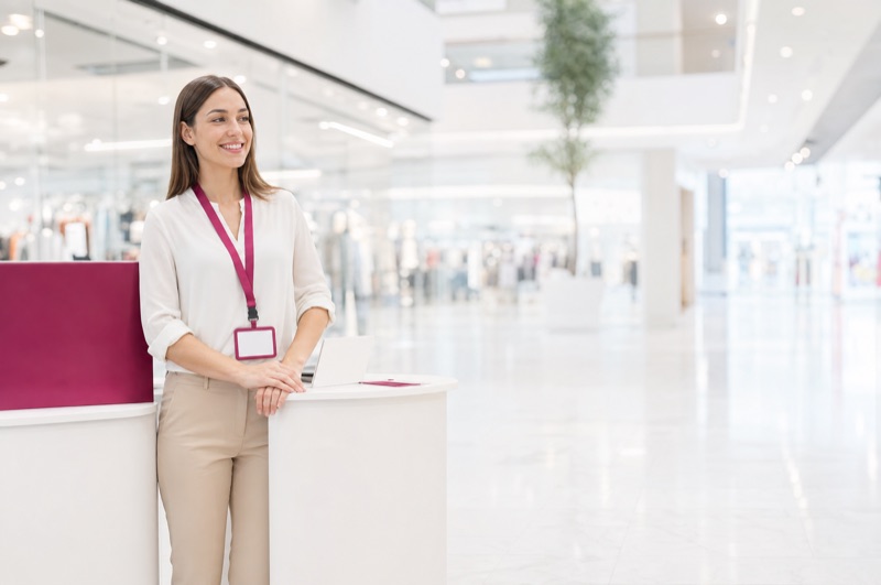 Junge Promoterin an einem weißen Stand in einem hellen Einkaufszentrum